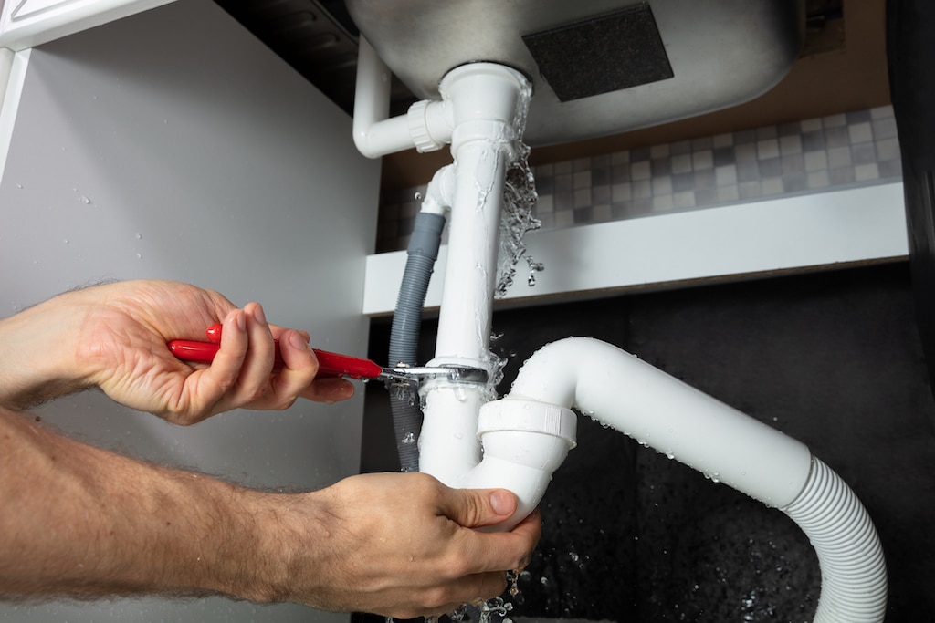 Person doing plumbing repair on sink pipe with adjustable wrench. 