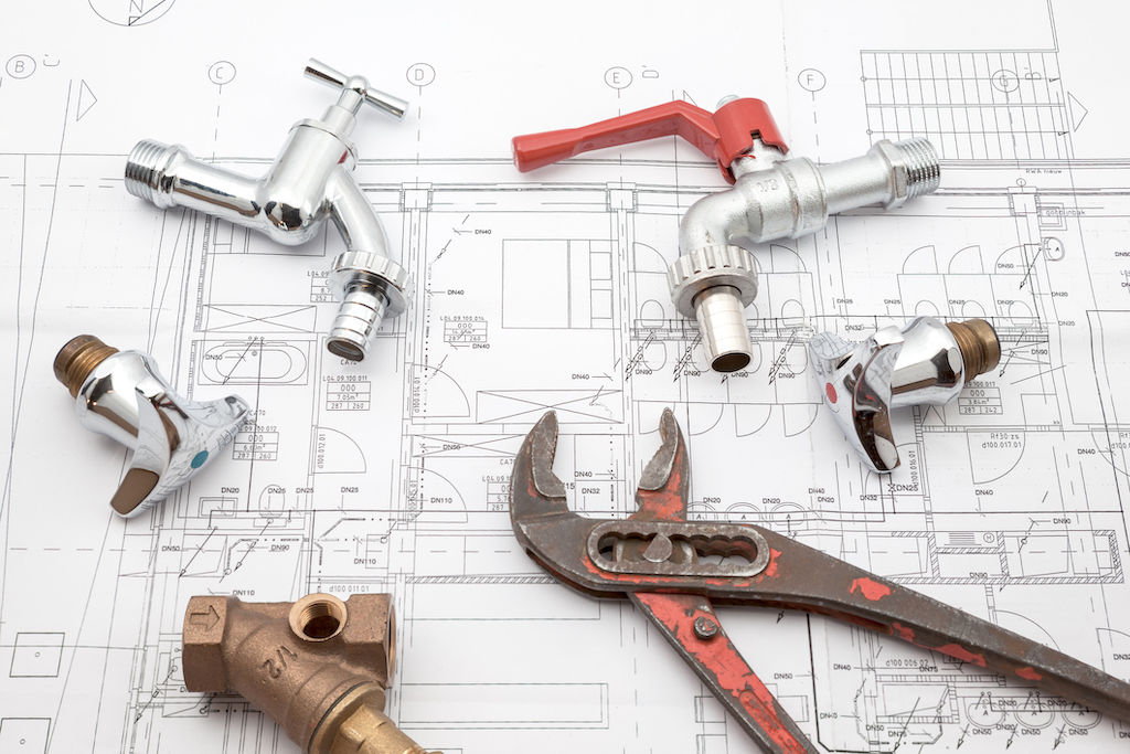 Various plumbing tools sitting on house plans for plumbing service.