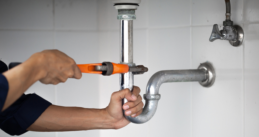 Plumber working on drainpipe in bathroom with orange wrench, plumbing service.