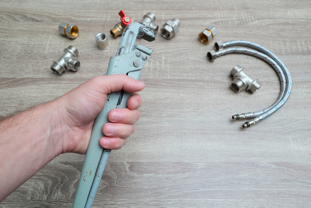 Person holding wrench with various plumbing tools on floor. | catch basin cleaning