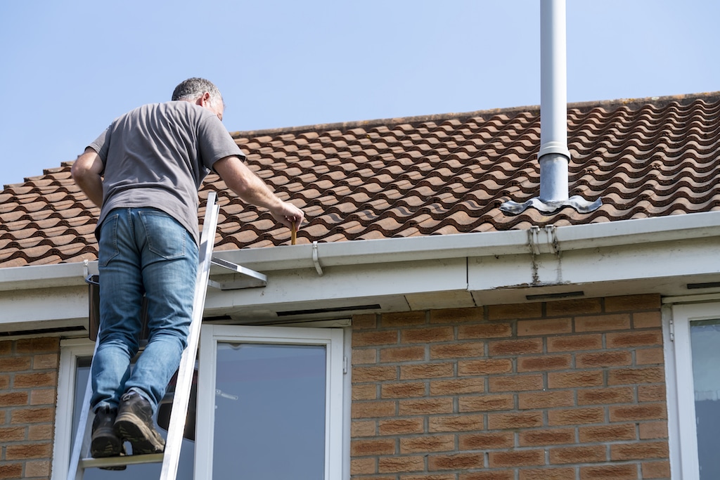 Older man installing gutter on home, DIY. | roof drain