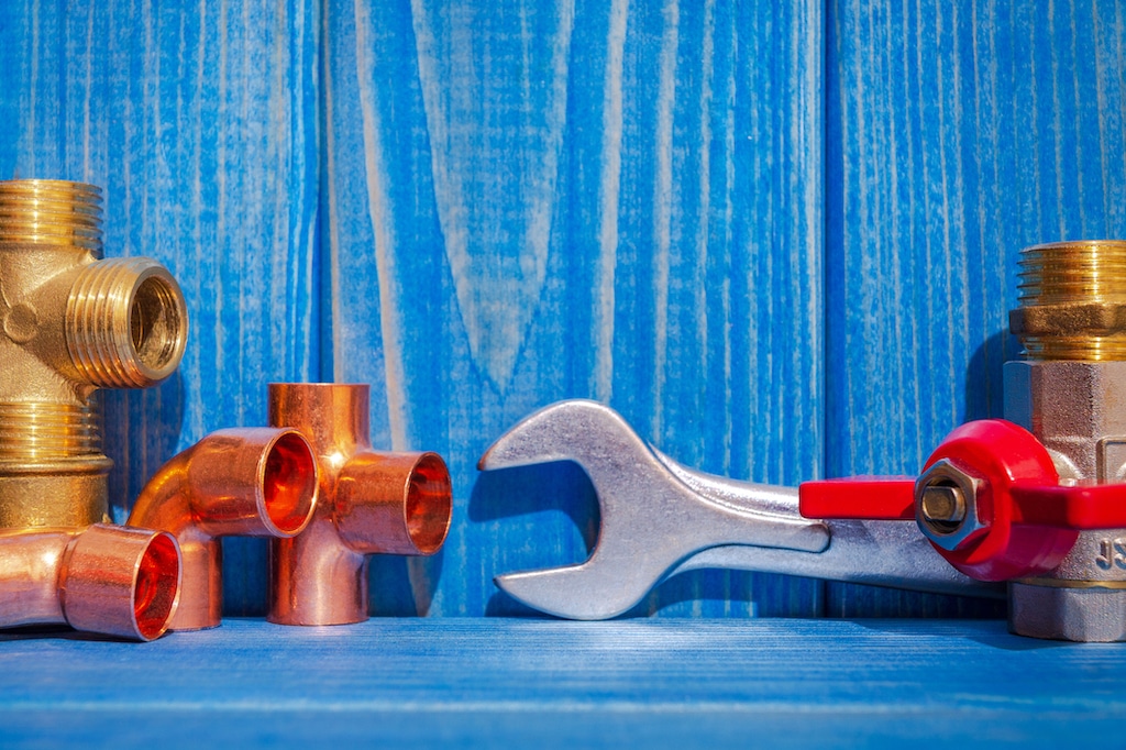 Copper parts and wrench on blue wooden backdrop. | Madisonville's Premier Plumbing Services
